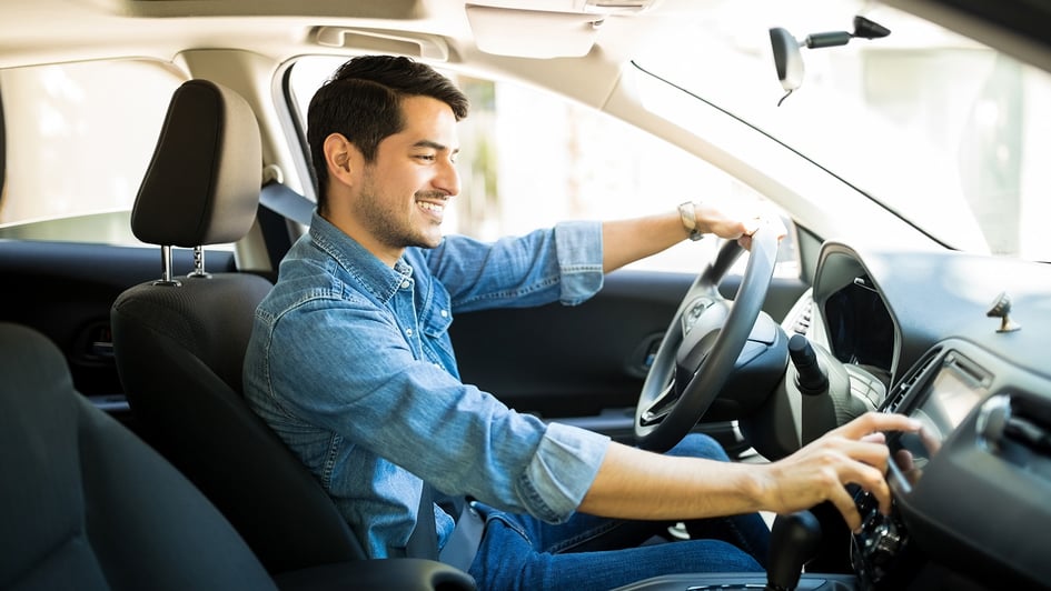 Conductor sonriente interactuando con la tecnología de la pantalla central de un carro híbrido moderno en Colombia, representando la movilidad eficiente para empresas y el 'Top 5 carros híbridos más vendidos'