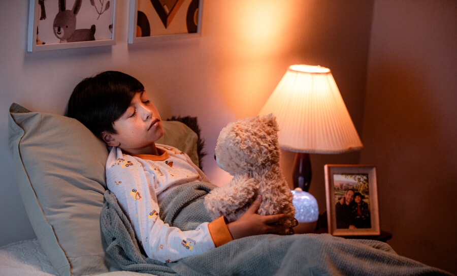 Niño durmiendo plácidamente en su cama abrazando un oso de peluche en la noche