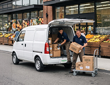 Dos trabajadores descargando cajas de una van blanca frente a un supermercado, ilustrando la movilidad eficiente de Renting Colombia para el sector comercio