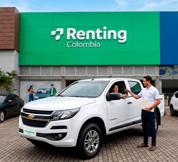 Asesor entregando las llaves de una camioneta blanca a una clienta frente a la sede de Renting Colombia, ilustrando el respaldo en soluciones de renta de carros para empresas