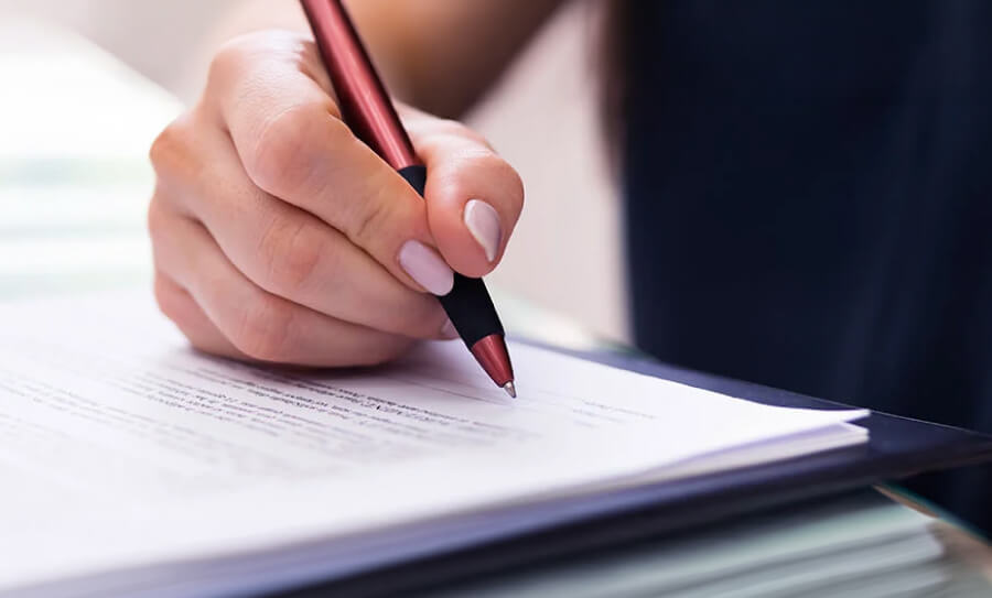 Primer plano de una mano firmando un documento, ilustrando la lectura y aceptación de los términos y condiciones de uso del sitio web